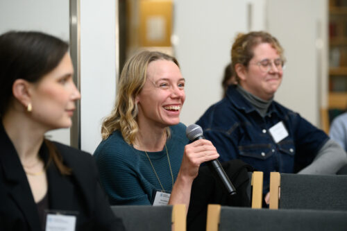 In the picture, a smiling woman is speaking into a microphone.