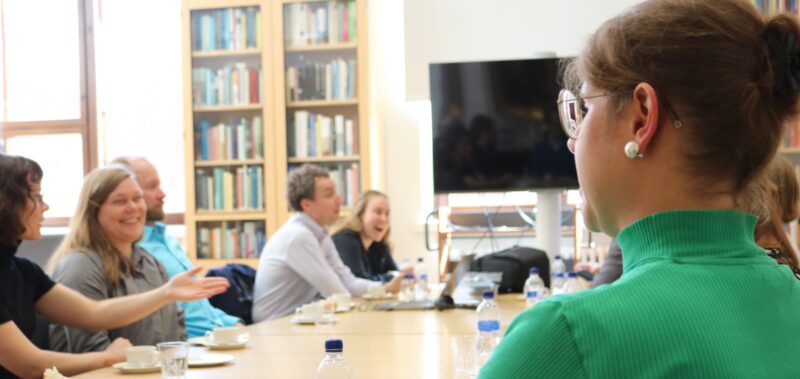 Ihmisiä istumassa ja keskustelemassa pöydän ympärillä.