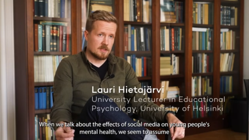 A screenshot from a video. University lecturer Lauri Hietajärvi talking. The subtitles in English say "When we talk about hte effects of social media on young people's mental healt, we seem to assume"